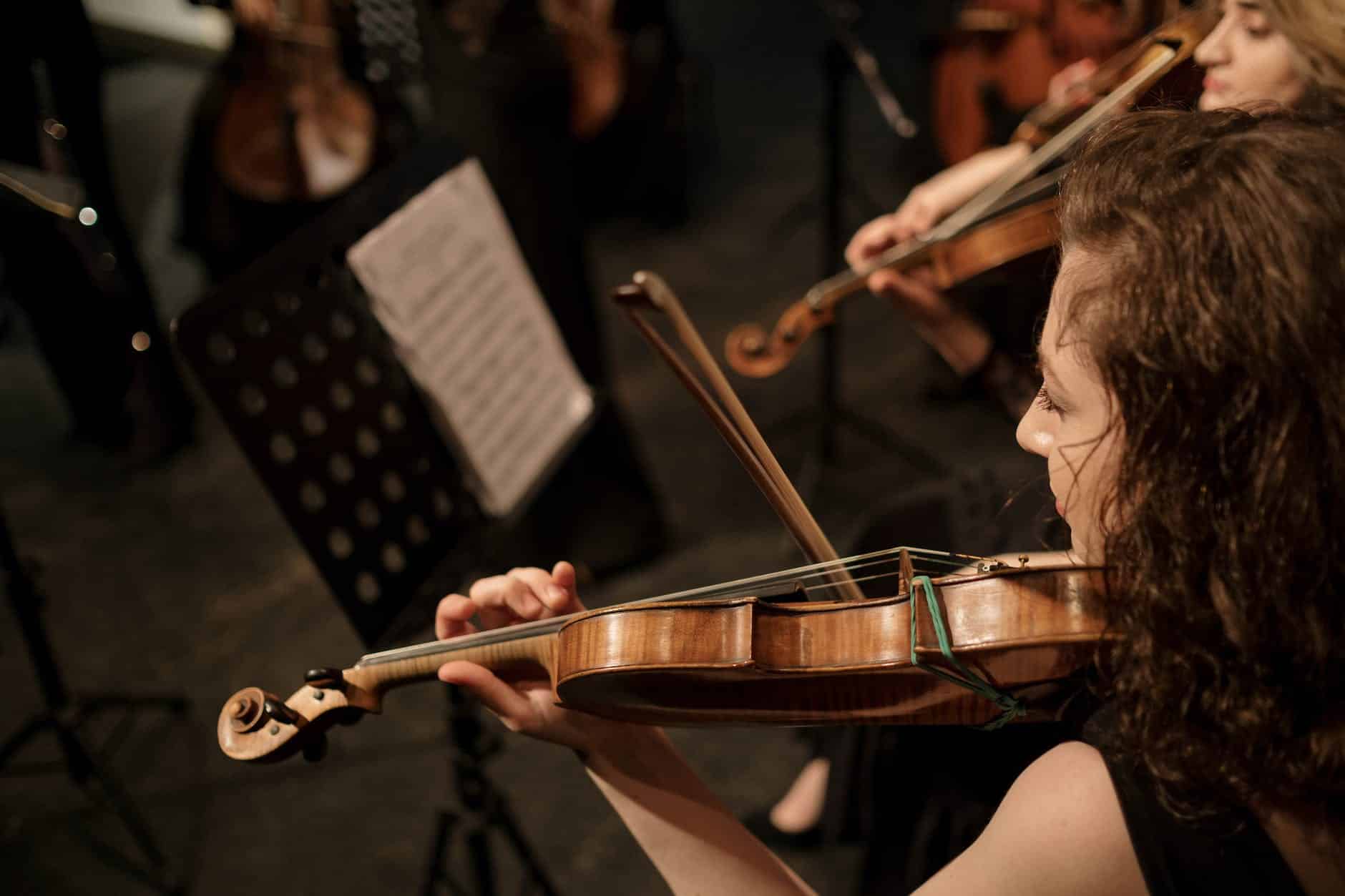 brunette woman playing on violin in orchestra