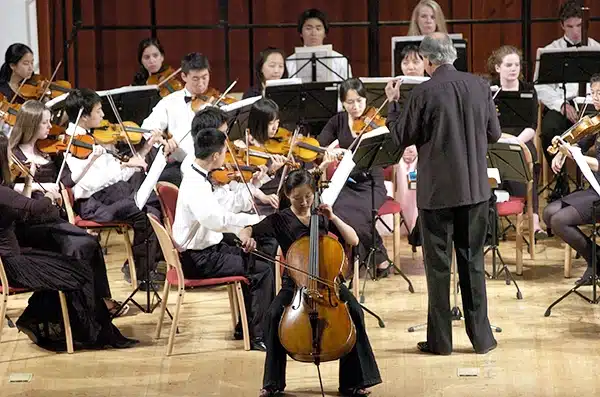 Conductor leading an orchestra with a cellist seated at the front of the ensemble